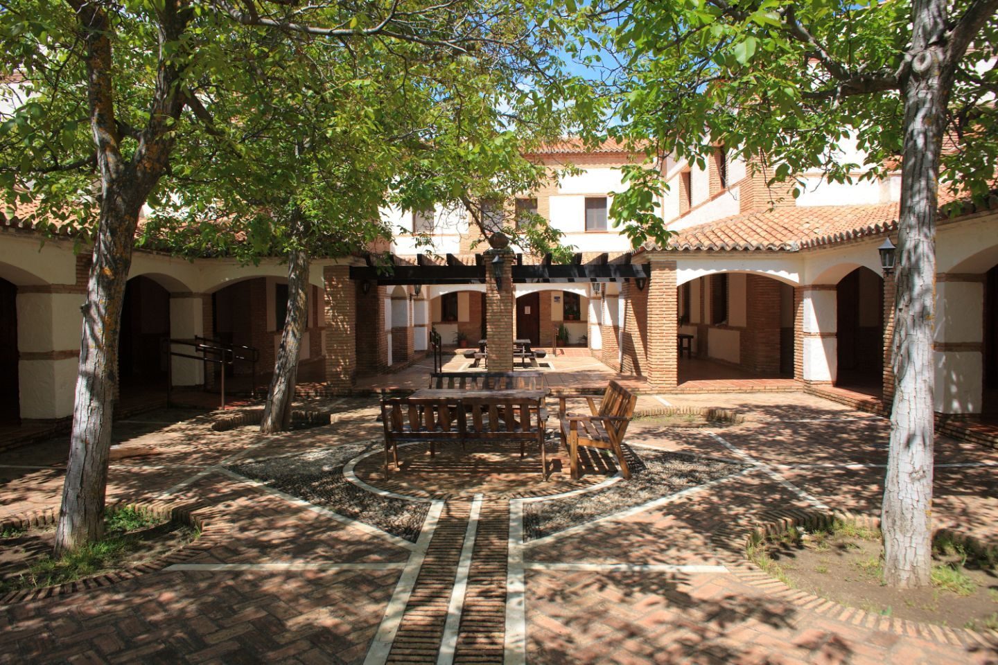 Patio empedrado con nogales y bancos de madera